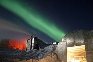 A full moon and 25 second exposure allowed sufficient light into this photo taken at Amundsen-Scott South Pole Station during the long Antarctic night. The new station can be seen at far left, power plant in the center and the old mechanic's garage in the lower right. Red lights are used outside during the winter darkness as their spectrum does not pollute the sky, allowing scientists to conduct astrophysical studies without artificial light interference. The green light in the sky is the aurora australis.