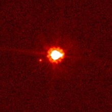 Immagine rossastra in cui un grande punto bianco centrale con un alone rosso è accompagnato da uno più piccolo.