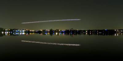 nightshot of a plane over a pond. You can see the landing and position lights as stripes.